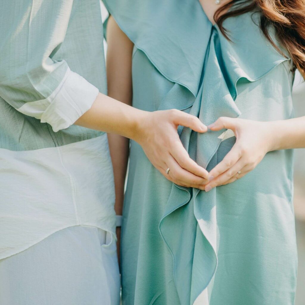 Man and pregnant woman making heart shape with hands over belly.